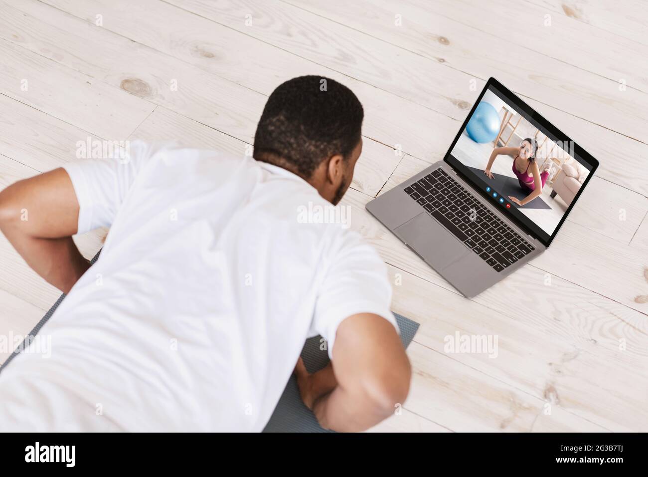 Black Young Man fare formazione online con il laptop a casa, irriconoscibile guy afroamericano fare esercizio Plank mentre si dispone di videochiamata con FEMA Foto Stock