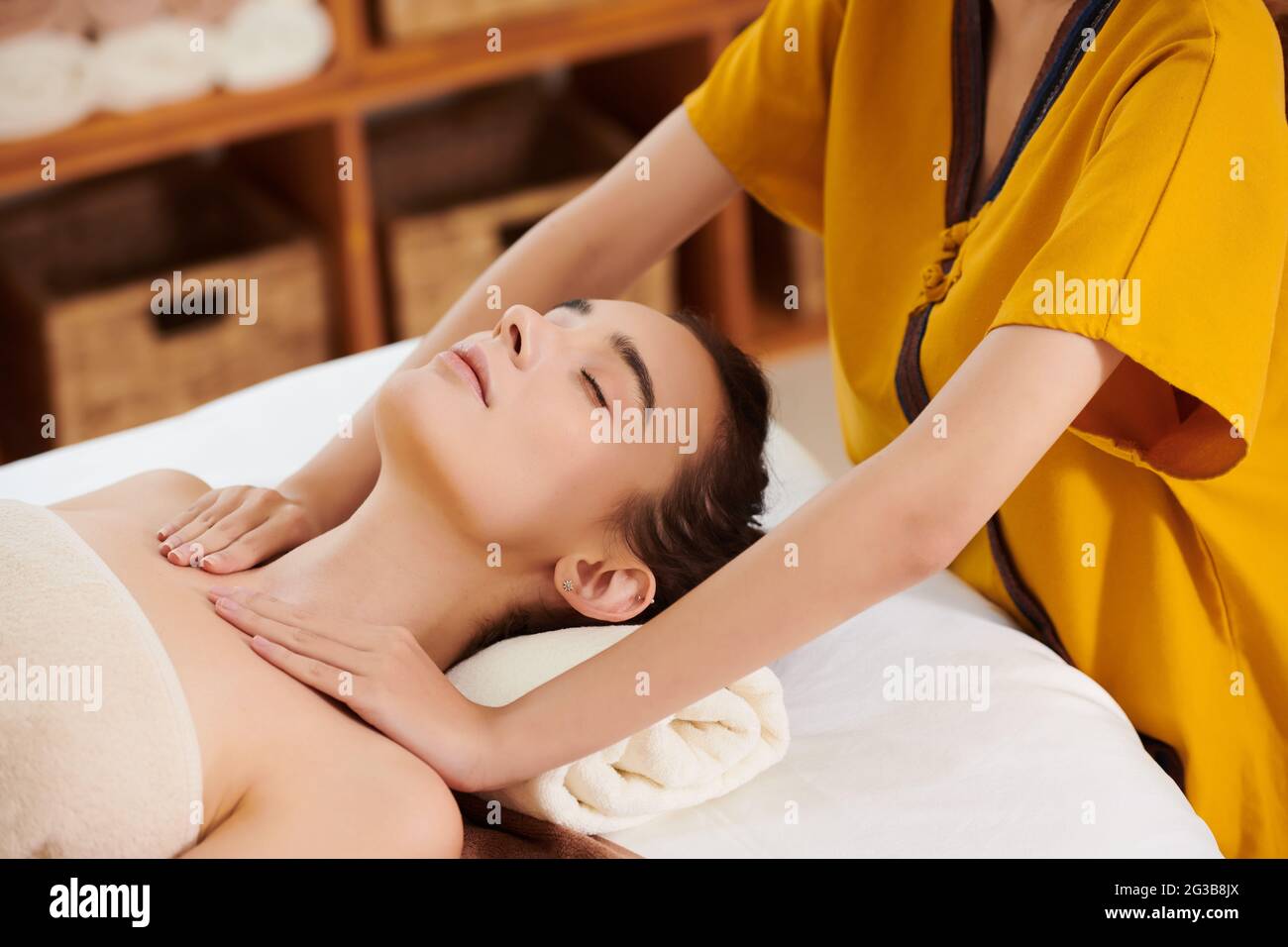 Primo piano del terapeuta che fa massaggio alla giovane donna mentre lei si steso sul letto con i suoi occhi chiusi Foto Stock