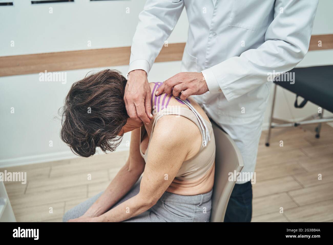 Medico che utilizza il metodo di applicazione del nastro cinesiologico per il dolore al collo Foto Stock