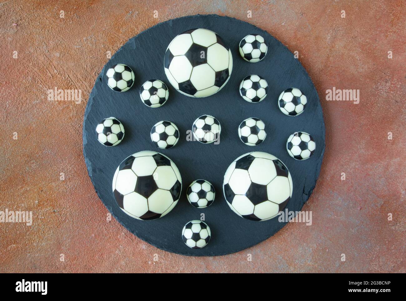 Palline da calcio classiche bianche e nere su un piatto da portata rotondo nero - torte da dessert fatte di cioccolato al latte bianco e nero sullo sfondo del campo Foto Stock
