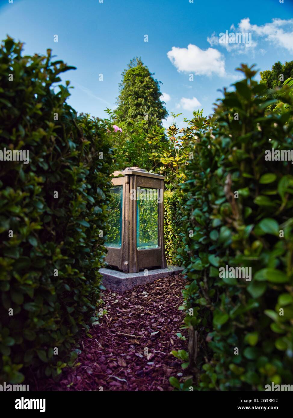 Una lanterna circondata da una siepe, attraverso la quale un sentiero stretto conduce sotto il cielo blu Foto Stock