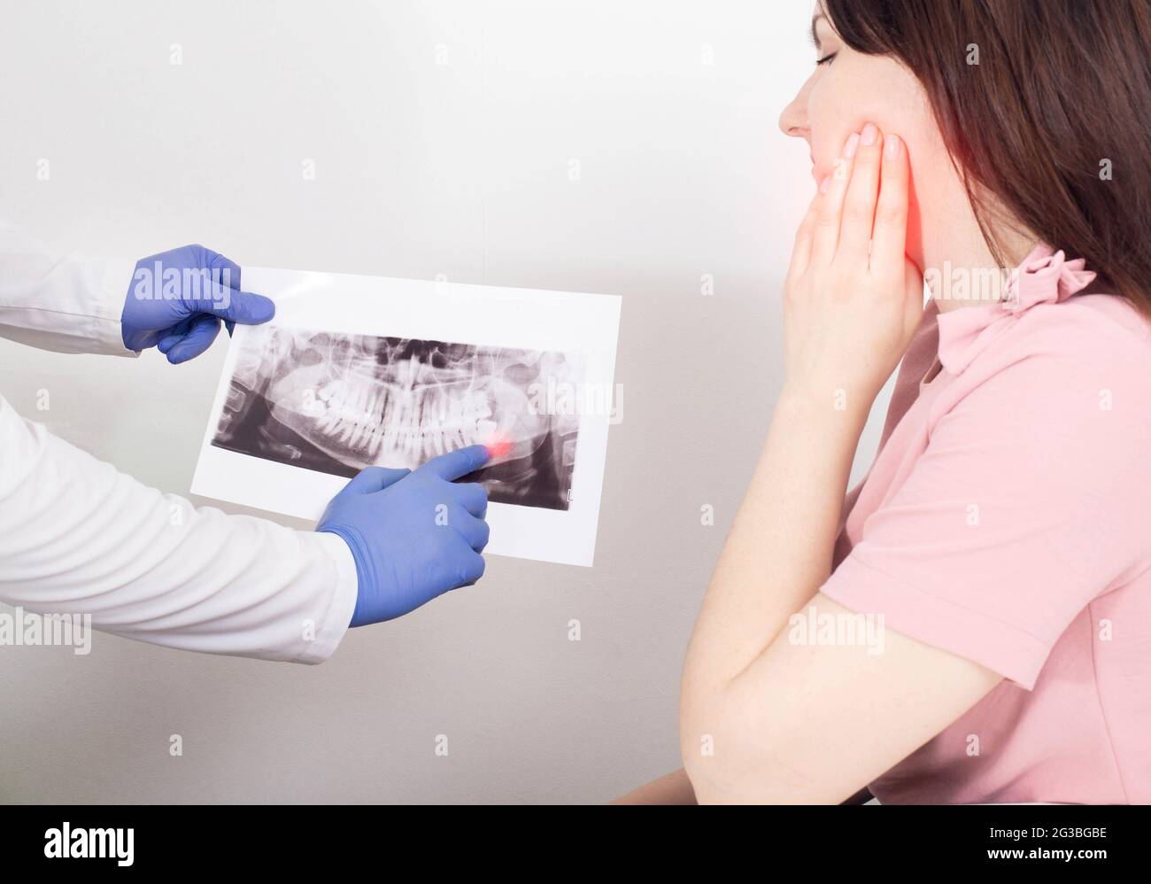 Un medico dentista sta tenendo un'immagine radiografica panoramica di una paziente femminile che ha una cisti dentale infiammata, un neoplasma. Rimozione di una cisti dentale, malig Foto Stock