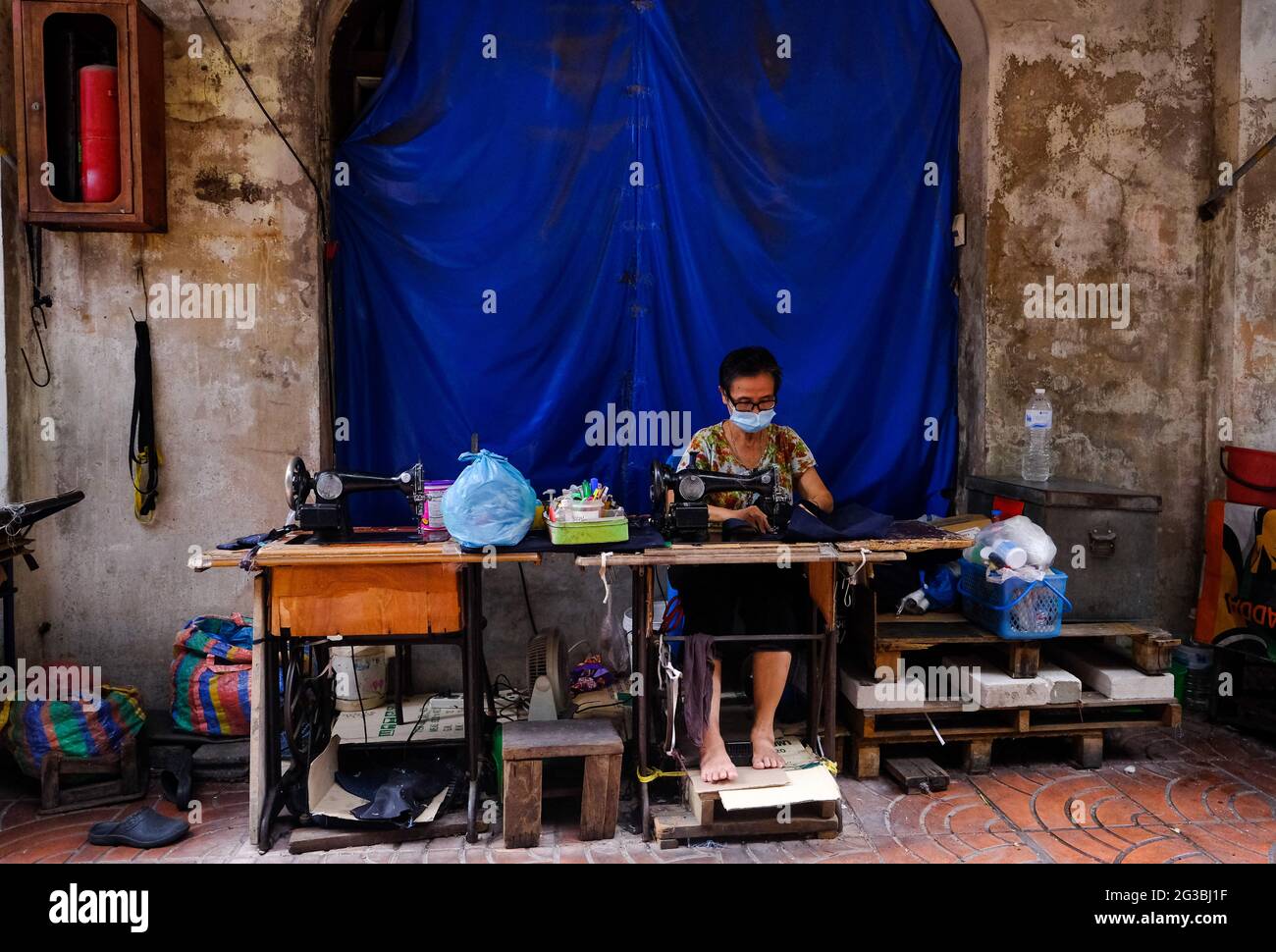 Una donna usa una macchina da cucire al suo negozio di sarto all'aperto situato in un vicolo stretto a Chinatown, Bangkok, Thailandia Foto Stock