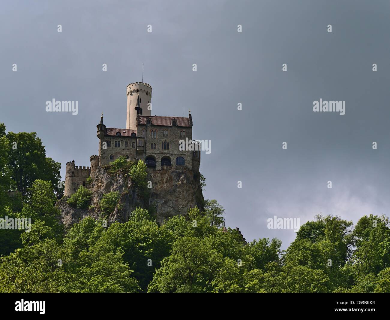Splendida vista ad angolo basso del popolare castello di Lichtenstein situato sulla scarpata dell'Alb Svevo, Germania con foresta verde in primavera e cielo nuvoloso. Foto Stock