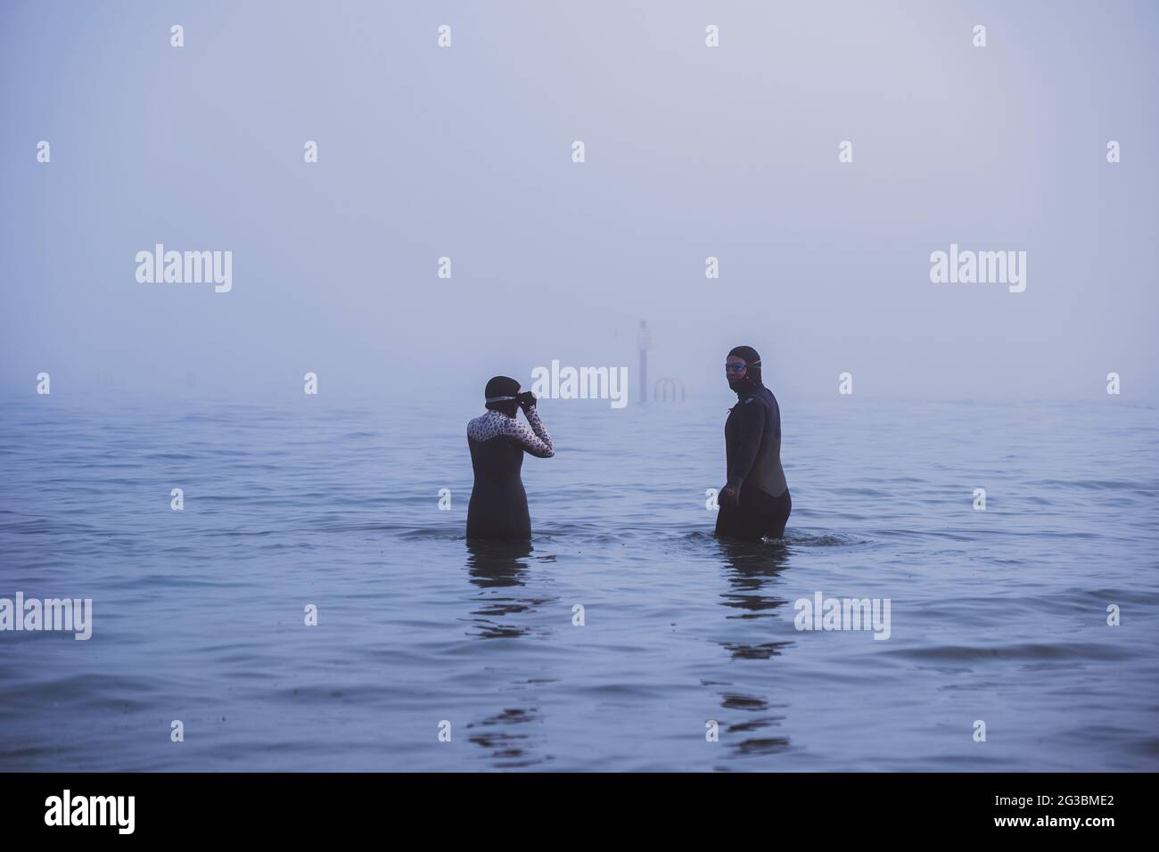 Una coppia che indossa mute va per una nuotata in mare nel Regno Unito in una mattina nebbiosa. Foto Stock