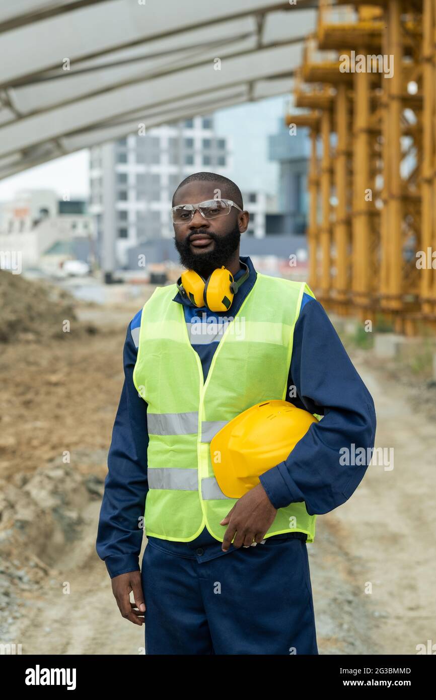 Giovane costruttore africano di sesso maschile in uniforme in piedi sul sito di costruzione Foto Stock