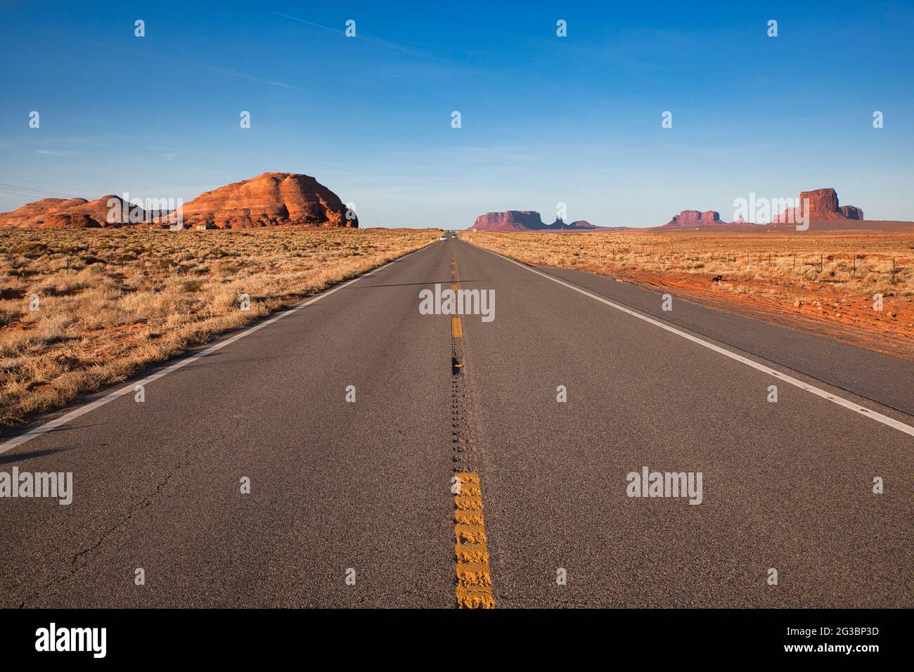 Vista lungo un lungo tratto di strada attraverso il semi-deserto in Arizona sulla strada per Monument Valley con affioramenti rocciosi o buttes in lontananza, gli Stati Uniti Foto Stock