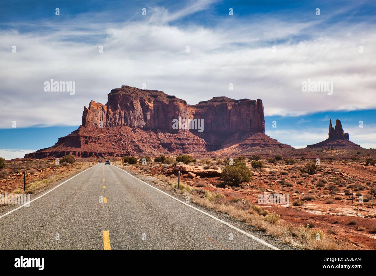 Un lungo tratto di strada principale con auto in lontananza e una vista spettacolare di una tipica roccia a picco con scogliere a strapiombo, in Monument Valley, Arizona, Stati Uniti Foto Stock