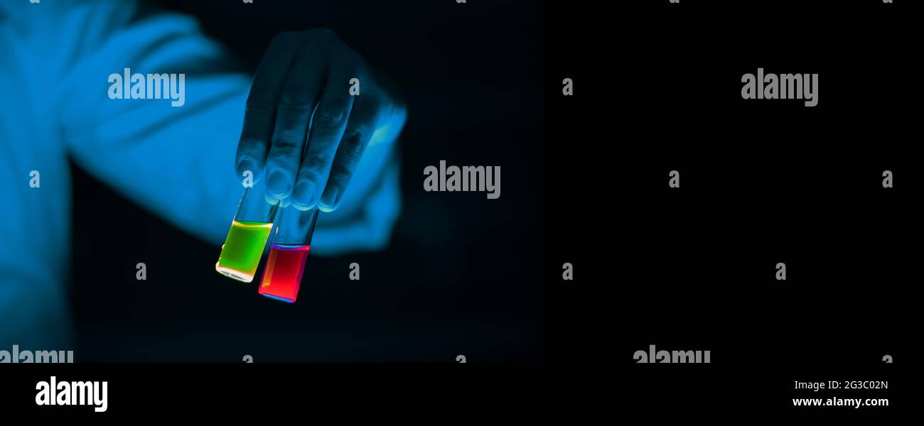 Una donna scienziata che tiene fiale di vetro per campioni di chimica organica in un laboratorio - radioattivo - fluorescenza. Uno sfondo nero dello spazio di copia. Io organico Foto Stock