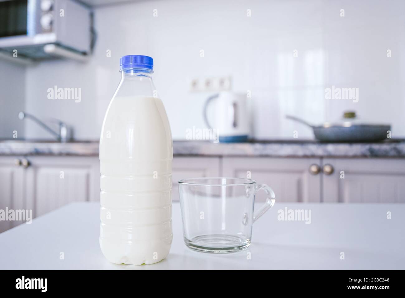 bottiglia di latte e una tazza di vetro vuota e pulita sul tavolo da cucina sullo sfondo una parete accogliente e luminosa della cucina. Foto Stock