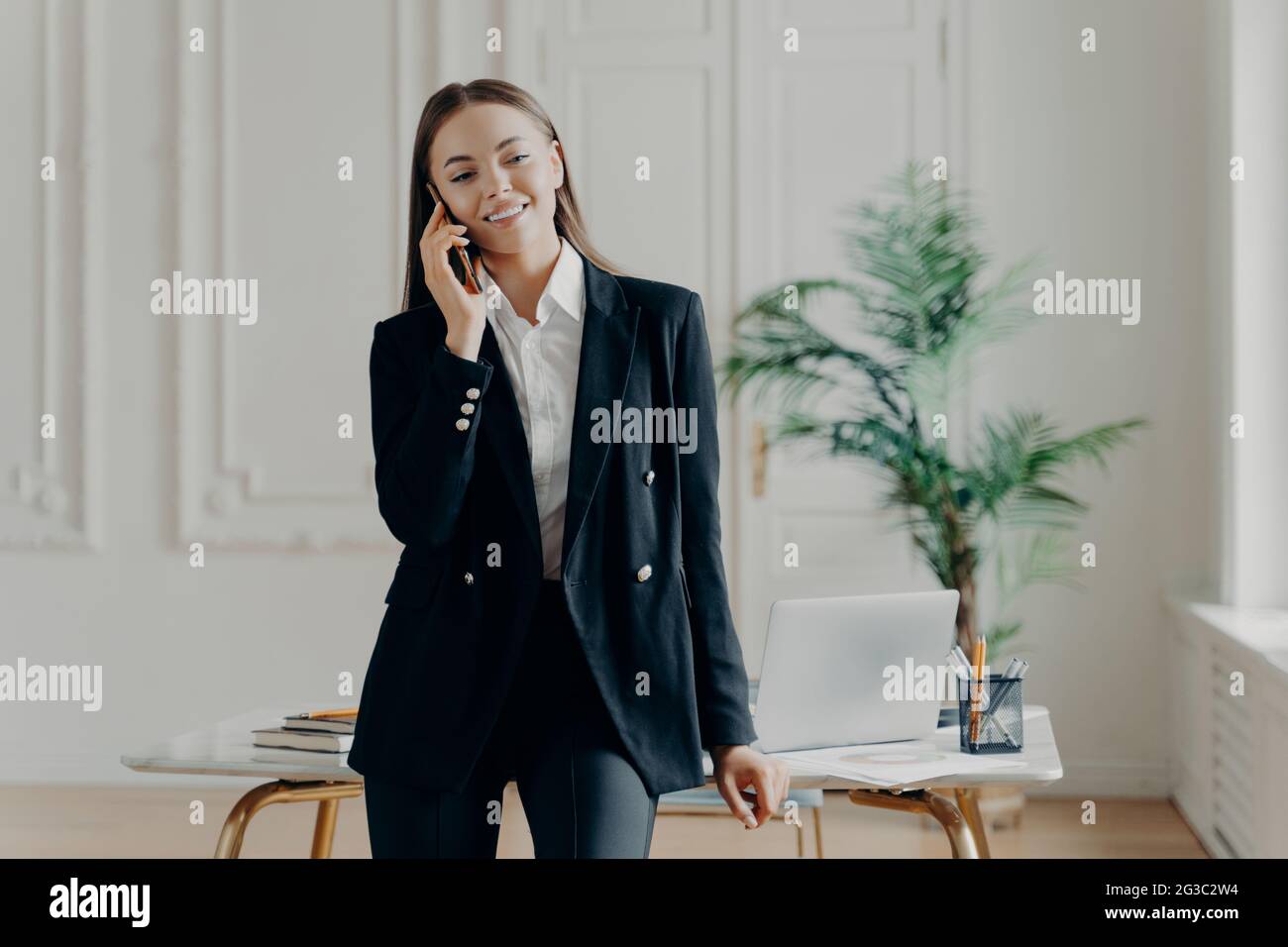 Sorridente giovane attraente donna d'affari in piedi e che parla al telefono Foto Stock