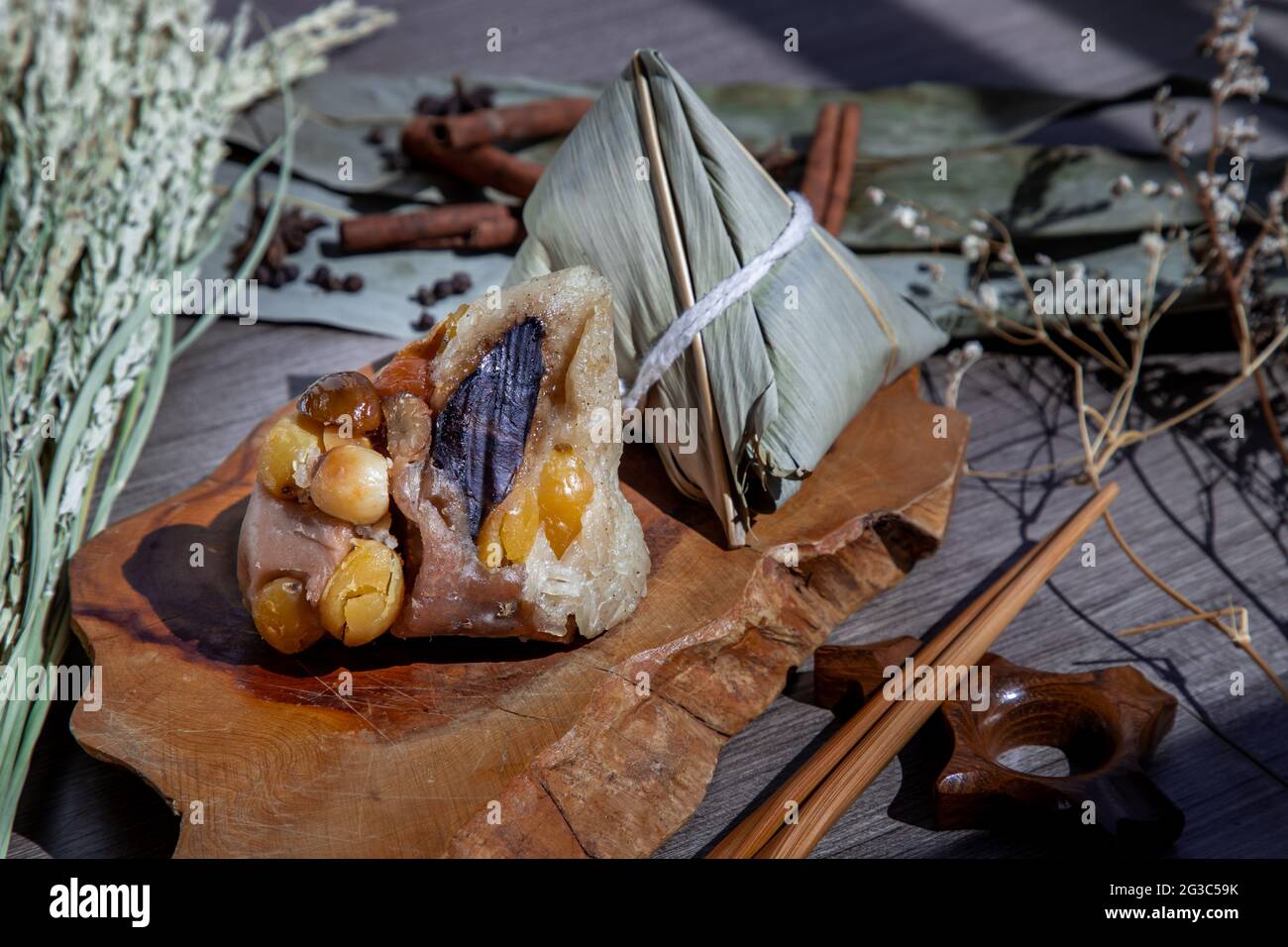 Gnocchi di riso cinese (Zongzi) a forma di piramide avvolto da foglie ingredienti su piastra di legno e bastoncini. Famoso cibo asiatico gustoso fatto a mano in drag Foto Stock