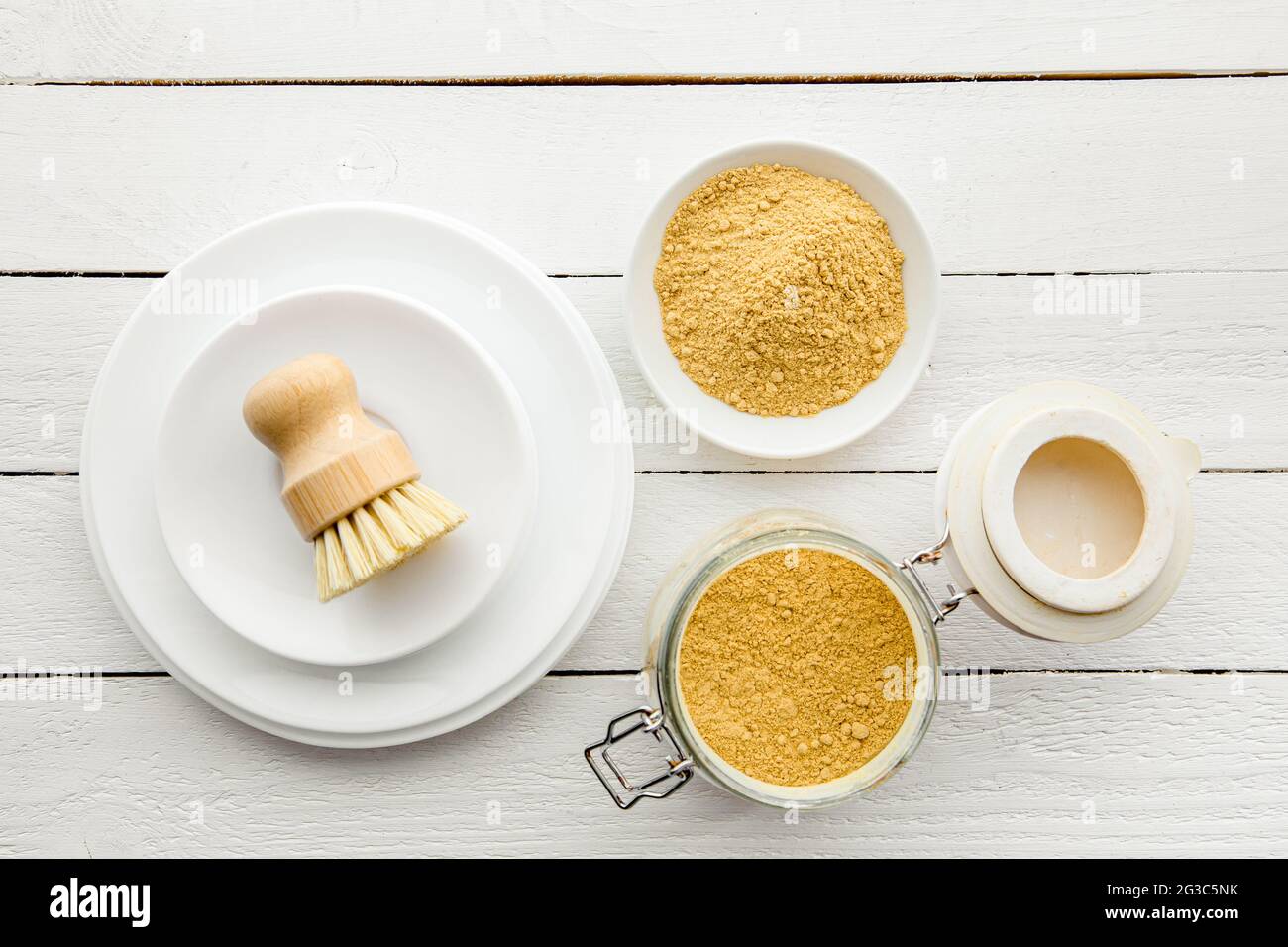 Lavare i piatti con il concetto di polvere di senape. Piastre bianche pulite con recipiente e vasetto di polvere di senape gialla e spazzola di lavaggio per piatti in legno e classe Foto Stock