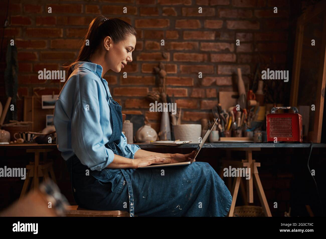 Felice sorridente elegante donna artigianale che indossa uniforme guardando allo schermo del notebook Foto Stock