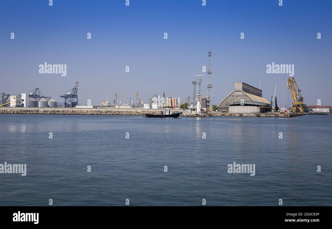 Porto - piccole imbarcazioni, gru, magazzini, banchina, silos, uccello contro il cielo blu Foto Stock