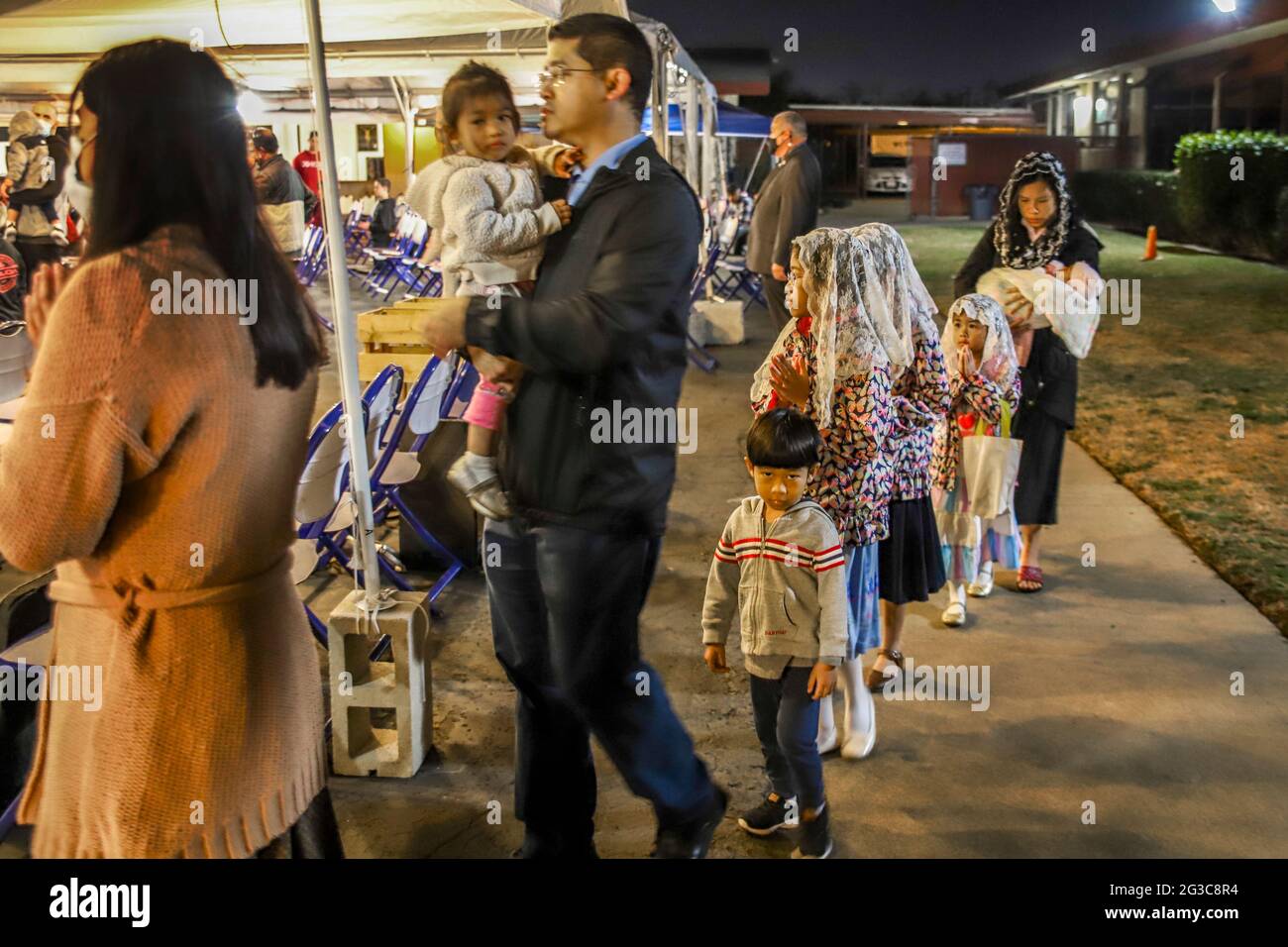 Un padre americano asiatico e i suoi figli arrivano a una messa di tenda all'aperto in una chiesa cattolica californiana. Note figlie più anziane in mantilla tradizionale Foto Stock