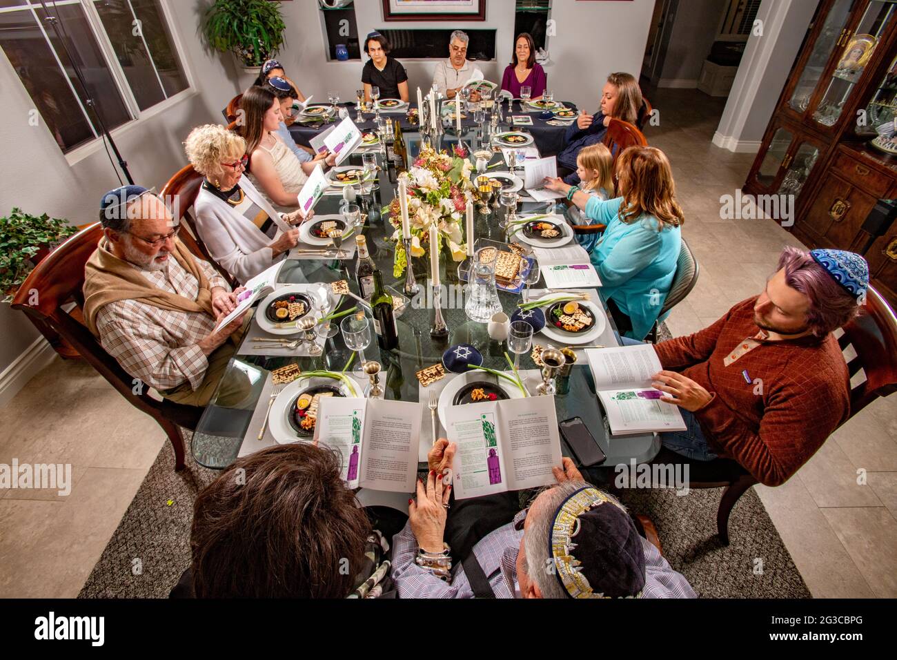 Al tradizionale tavolo da pranzo per un Seder Passover in una casa Ebraica della California Meridionale, gli ospiti leggono l'Haggadah, un testo ebraico che descrive Foto Stock