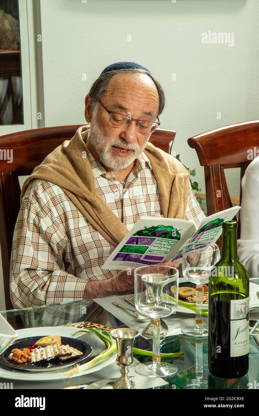 Al tradizionale tavolo da pranzo per un Seder Passover in una casa Ebraica della California Meridionale, un ospite legge l'Haggadah, un testo ebraico che descrive t Foto Stock