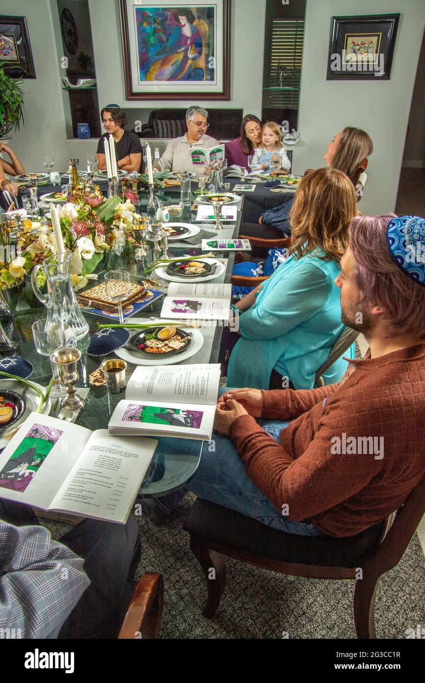 Al tradizionale tavolo da pranzo per un Seder Passover in una casa Ebraica della California Meridionale, gli ospiti leggono l'Haggadah, un testo ebraico che descrive Foto Stock