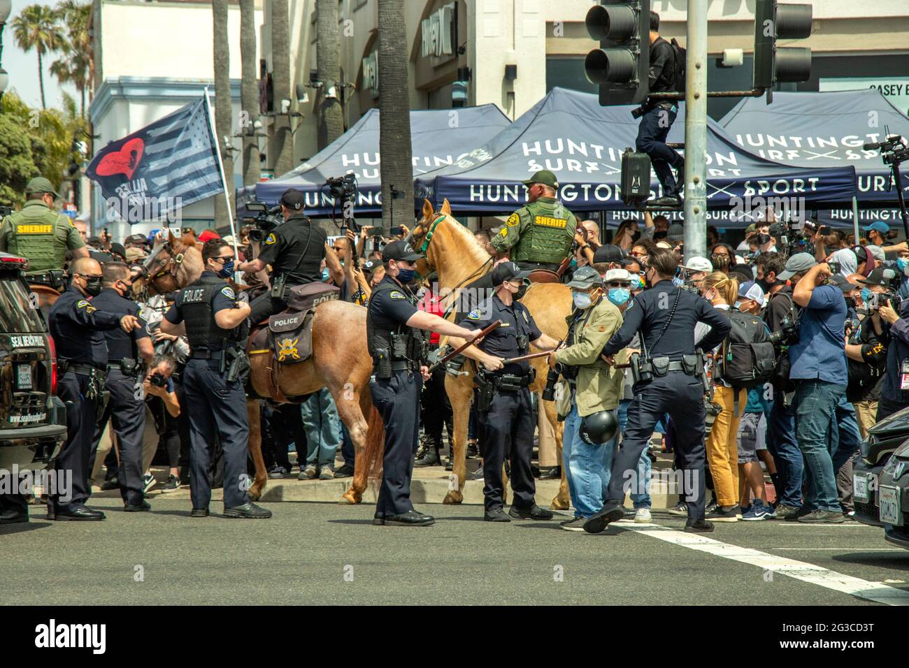 I sostenitori caucasici di Donald Trump marciano per protestare contro la sconfitta elettorale del 2020 a Huntington Beach, California, mentre la polizia li tiene confinati in una strada di corne Foto Stock