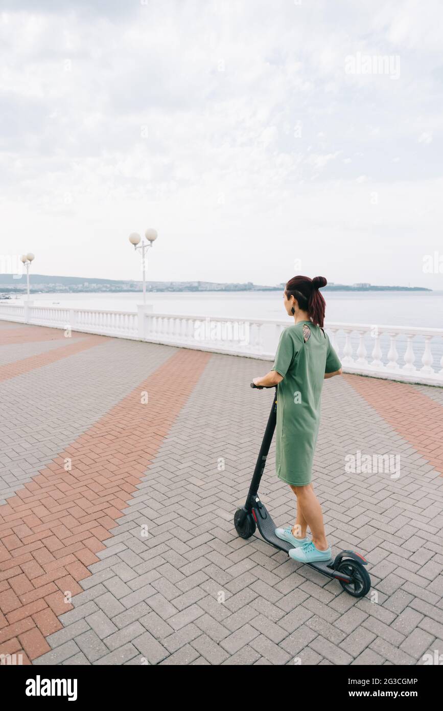 Giovane donna in un vestito guida un elettro scooter. Foto Stock