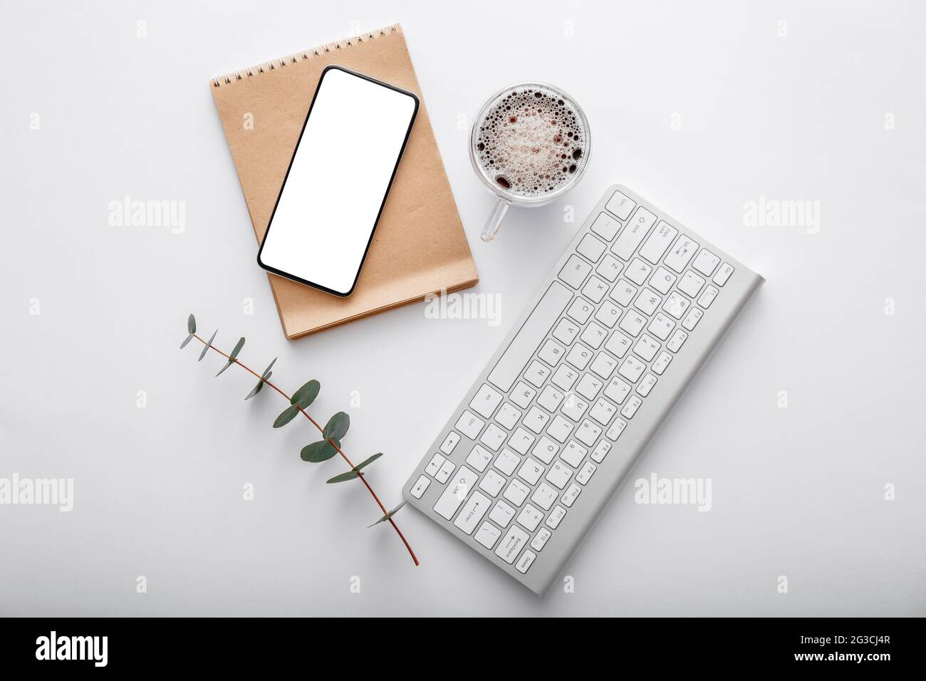 Smartphone mock-up con tastiera nota caffè tazza verde pianta su scrivania spazio di lavoro bianco. Vista dall'alto in piano. Telefono cellulare su un moderno spazio di lavoro Foto Stock