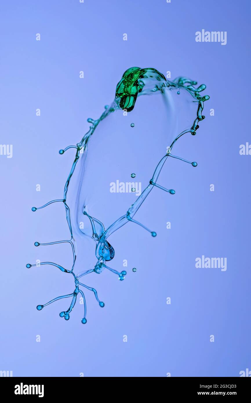 Due gocce d'acqua liberate dall'alto per incontrare un beccuccio di pressione dal basso, tutte colorate con colorante, per creare e forma interessante a mezz'aria Foto Stock