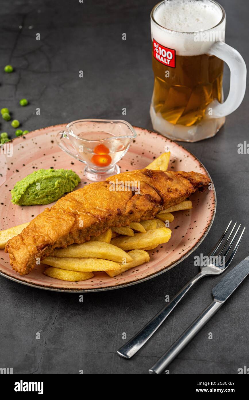 Pesce tradizionale britannico e patatine con purè di piselli, salsa di piselli e birra fredda. Foto Stock