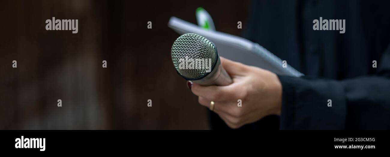 Giornalista femminile in azione alla conferenza stampa, tenendo microfoni e scrivendo note Foto Stock