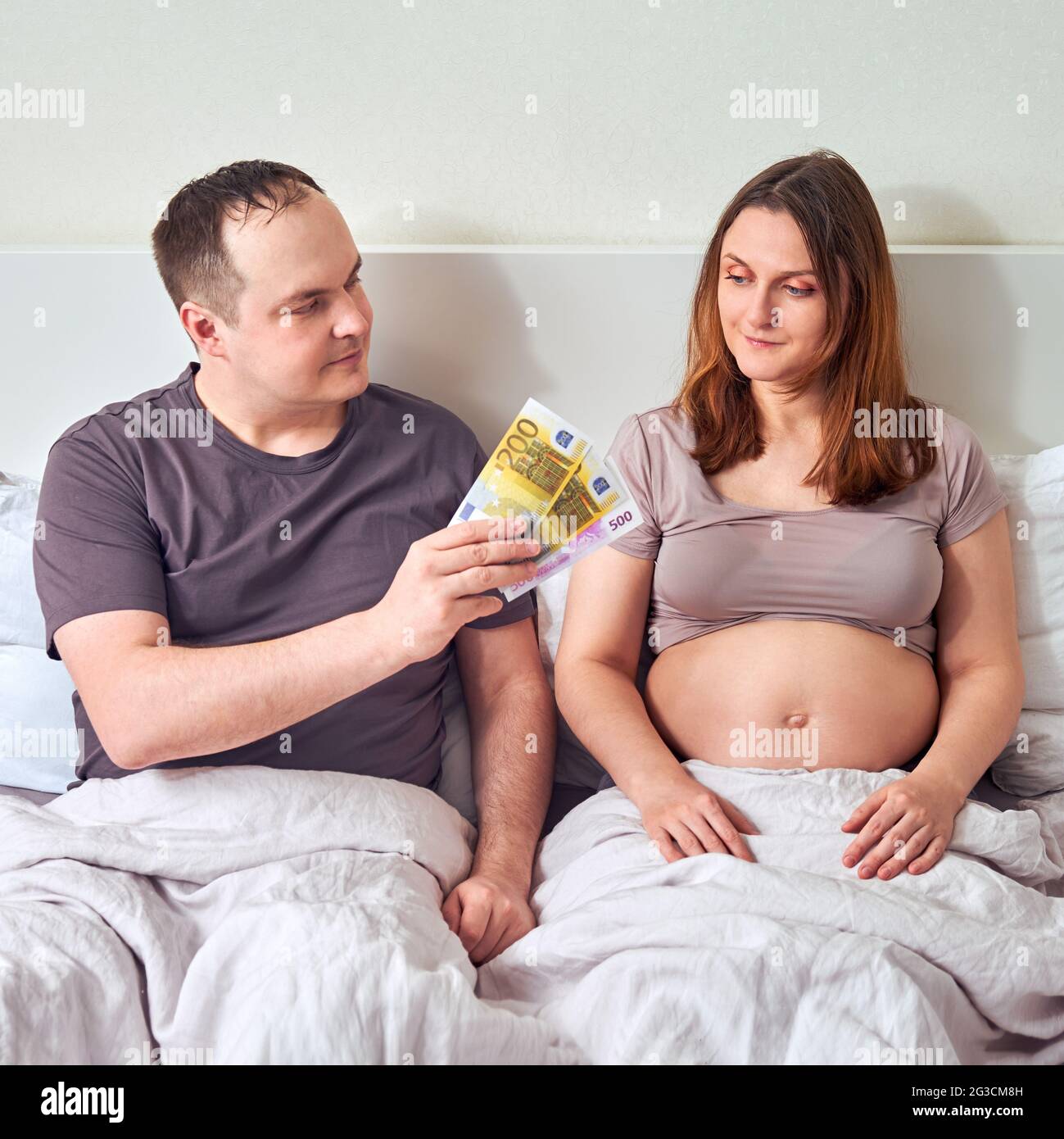 Il marito dà i soldi in euro nel letto della casa per la moglie incinta Foto Stock