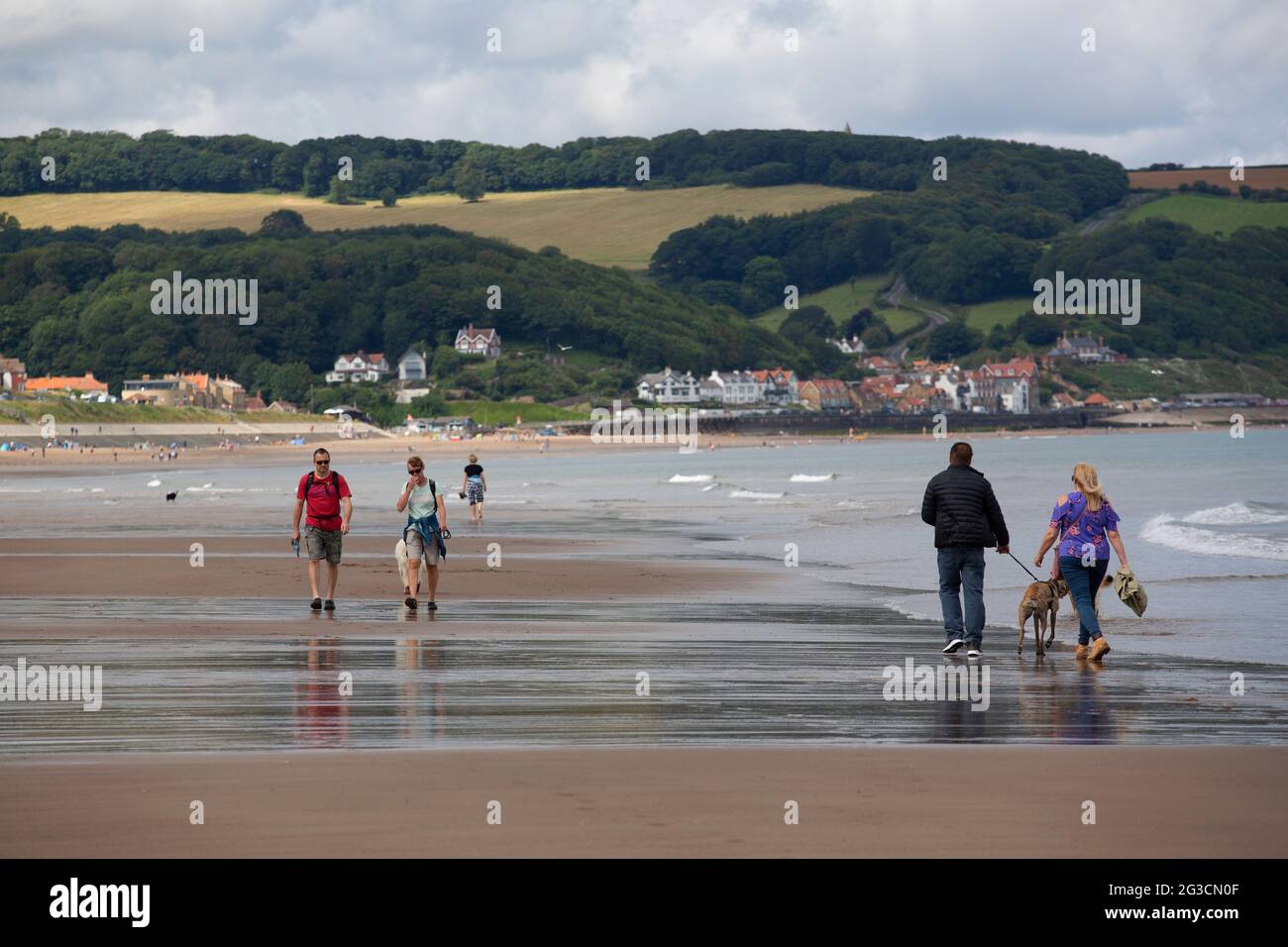 La gente passeggia lungo la spiaggia di Sandsend con la piccola cittadina di pescatori di Sandsend in lontananza nel North Yorkshire. Foto Stock
