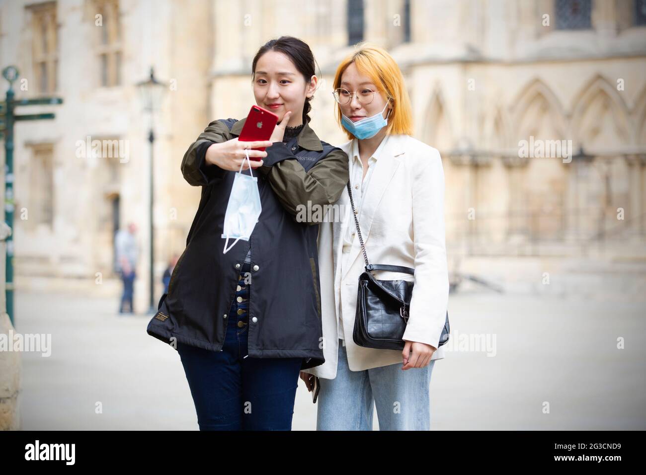 Gli studenti cinesi in maschere facciali protettive si mettono in posa mentre prendono ‘selfie’ di se stessi davanti alla York Minster di York, nel nord dello Yorkshire. York, Michigan Foto Stock