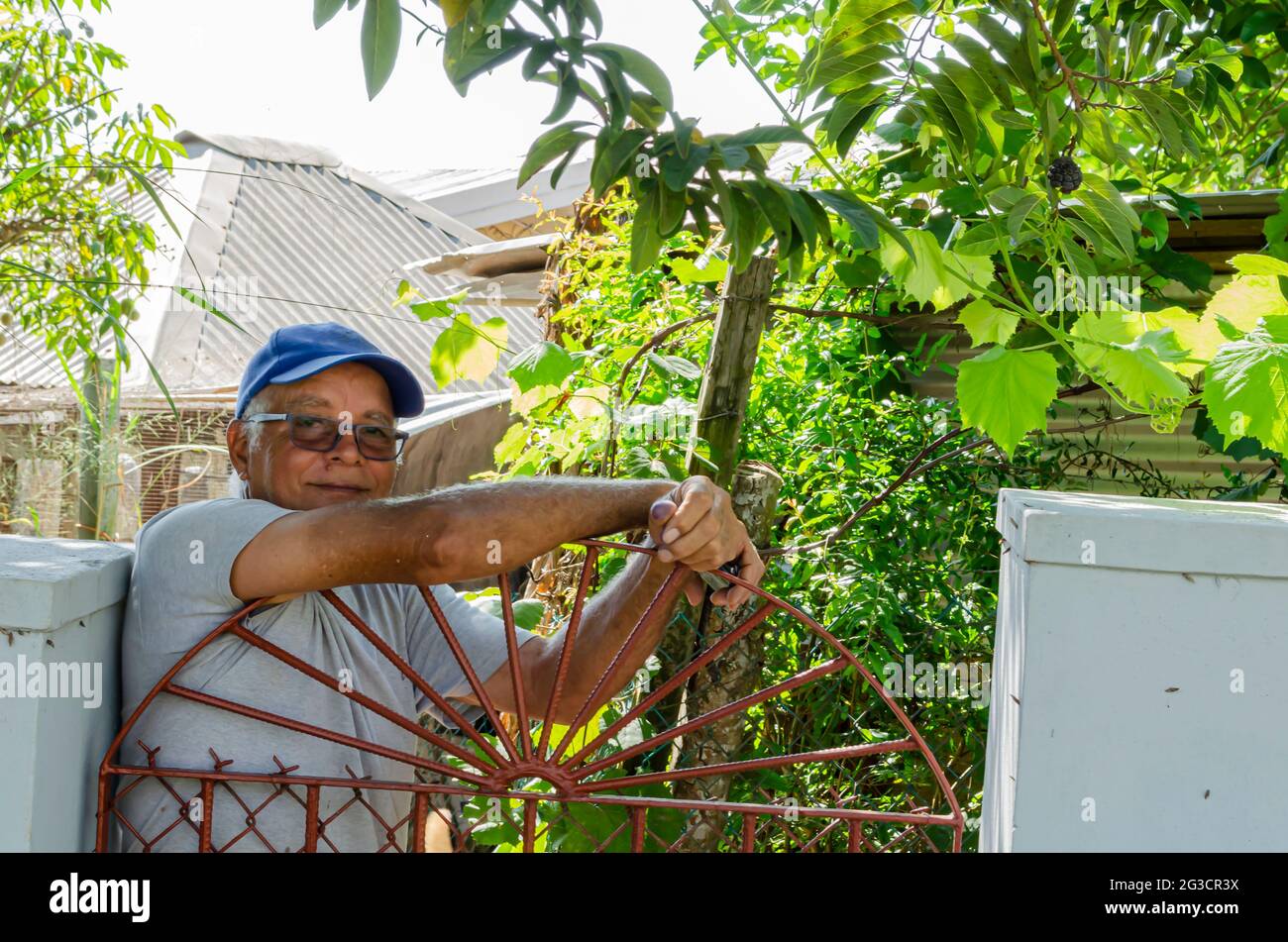 Uomo anziano giamaicano che guarda fuori da dietro il suo cancello Foto Stock