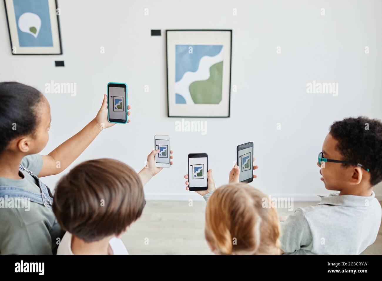 Vista ad alto angolo in diversi gruppi di bambini che tengono smartphone in galleria d'arte e scattano foto di dipinti, mondo digitale, spazio di copia Foto Stock