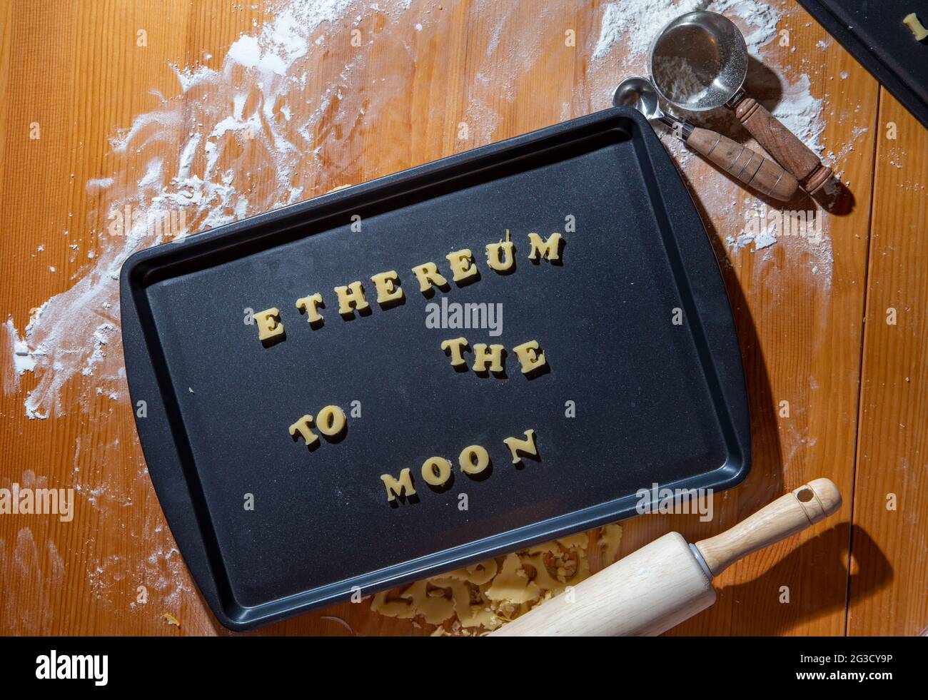 Biscotti non cotti su una piastra di cottura a forma di lettere con una frase che dice che una moneta popolare sta andando alla luna con farina e misurino cucchiaio Foto Stock