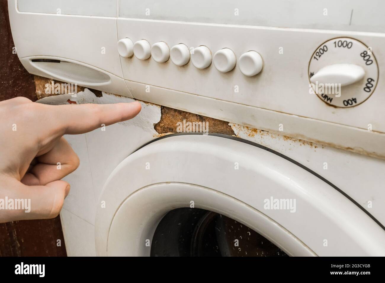 Una mano dell'uomo punta un dito su una traccia di ruggine accanto alla  tastiera anteriore di una vecchia lavatrice rotta. Il concetto di usura  degli elettrodomestici Foto stock - Alamy