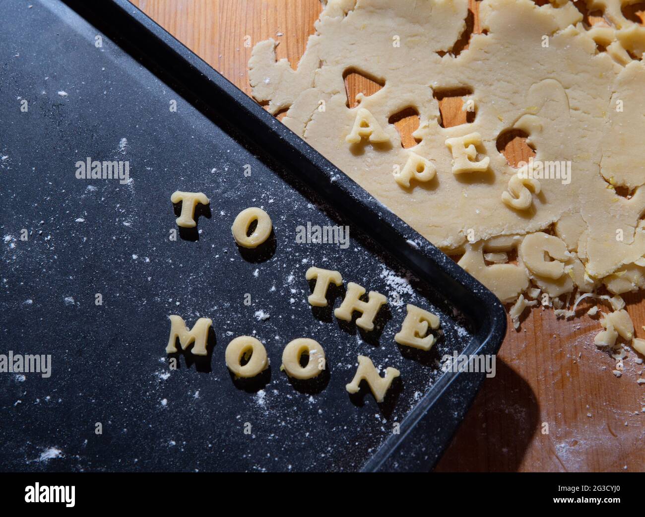 Biscotti grezzi su un piatto di cottura a forma di lettere con una frase che dice che le scimmie stanno andando alla luna con la farina e il cucchiaio graduato e il lig duro Foto Stock