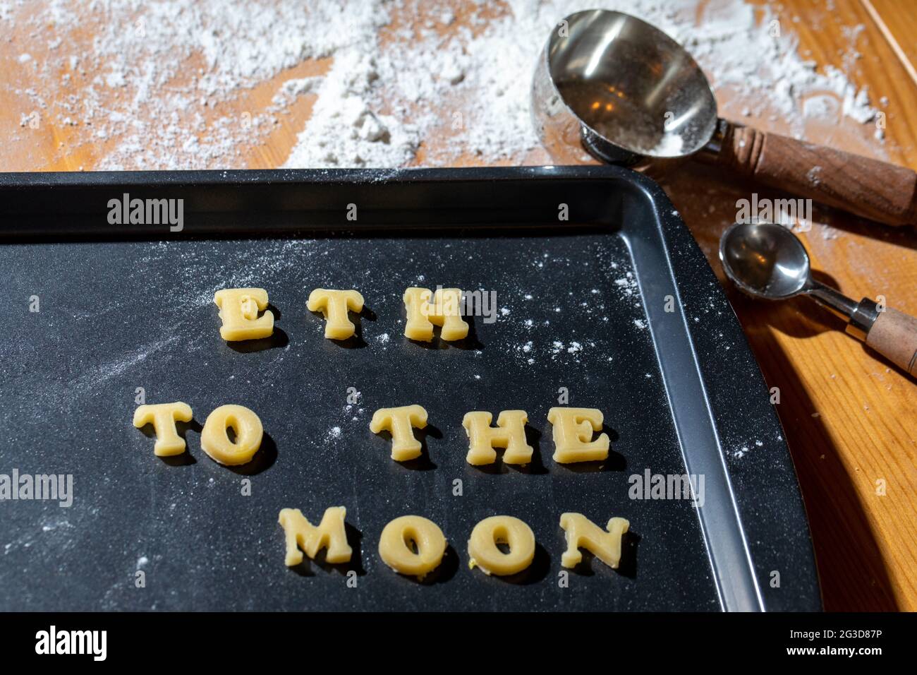 Biscotti crudi su un piatto di cottura a forma di lettere con una frase che dice che una moneta popolare sta andando alla luna con farina e misurino cucchiaio e. Foto Stock