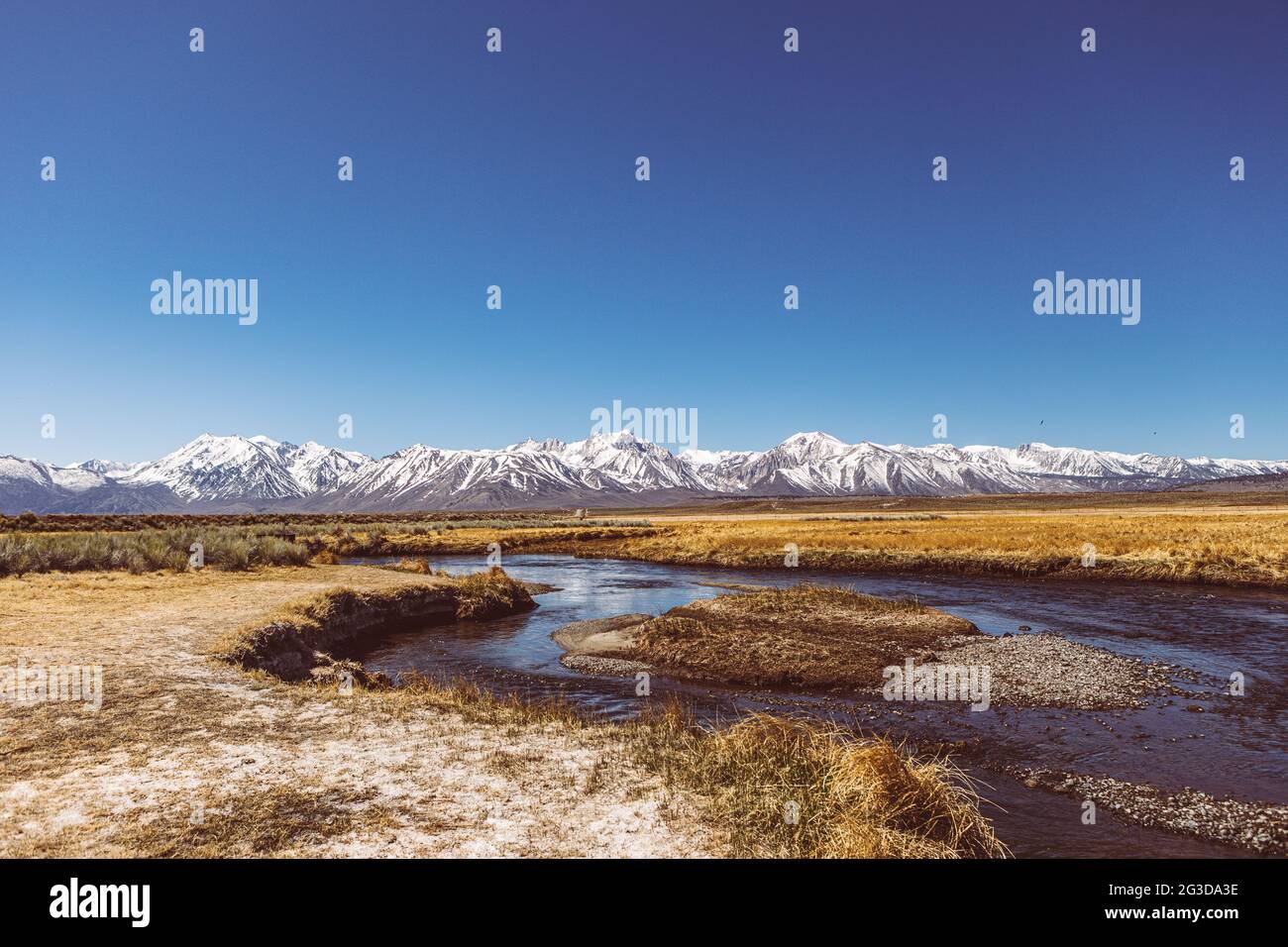 Il fiume corre attraverso una pianura arida contro il cielo blu delle montagne della Sierra Nevada Foto Stock