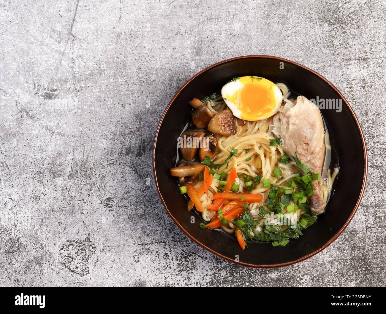 Ramen con funghi e pollo in una ciotola su uno sfondo scuro. Vista dall'alto, disposizione piatta Foto Stock