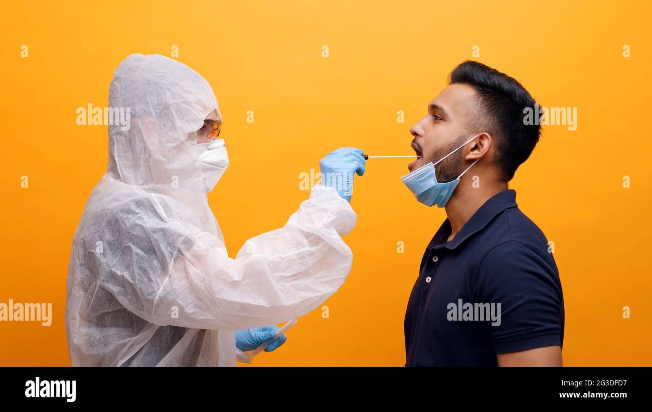 Operatore sanitario in tuta protettiva prendendo tampone orale da un ragazzo potenzialmente infetto. Corona PCR Virus Test con concetto di tampone. Monolocale con sfondo giallo. Foto di alta qualità. Foto Stock