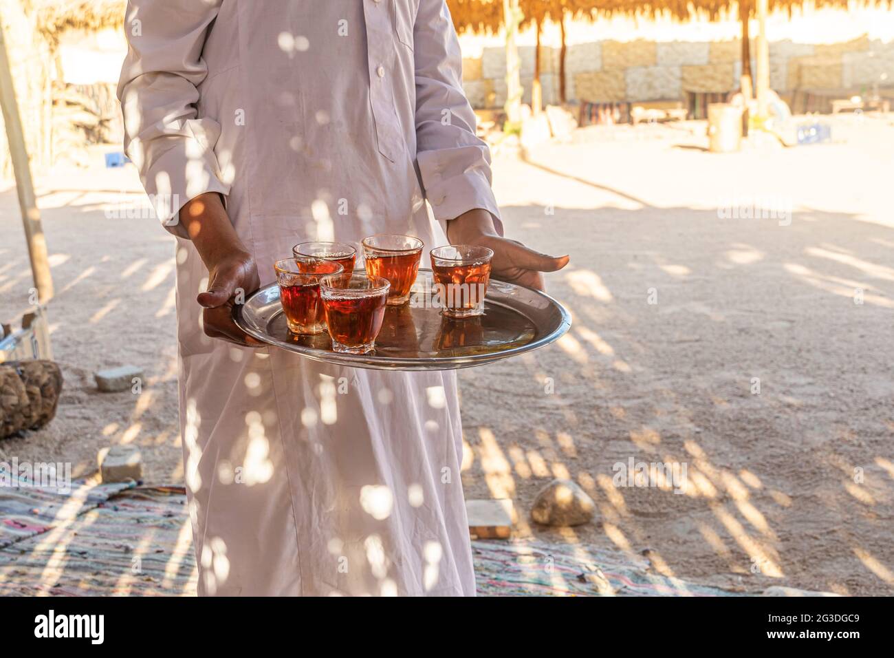 Un vassoio con tazze di tradizionale tè egiziano in mano al cameriere. Beduino dare il benvenuto a una tazza di tè con mandorle, Sinai. Foto Stock