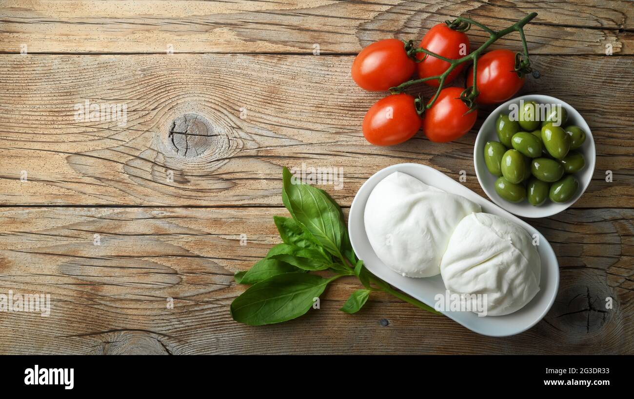 Due mozzarella di bufala, basilico, pomodori ciliegini e olive verdi su vecchio sfondo di legno, vista dall'alto, spazio per il testo. Foto Stock