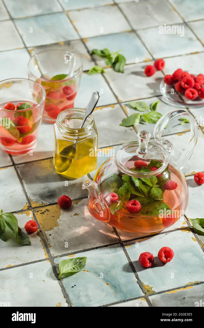 Tè caldo ai lamponi in teiera trasparente su un tavolo in pietra. Bacche fresche, menta, bicchiere Foto Stock