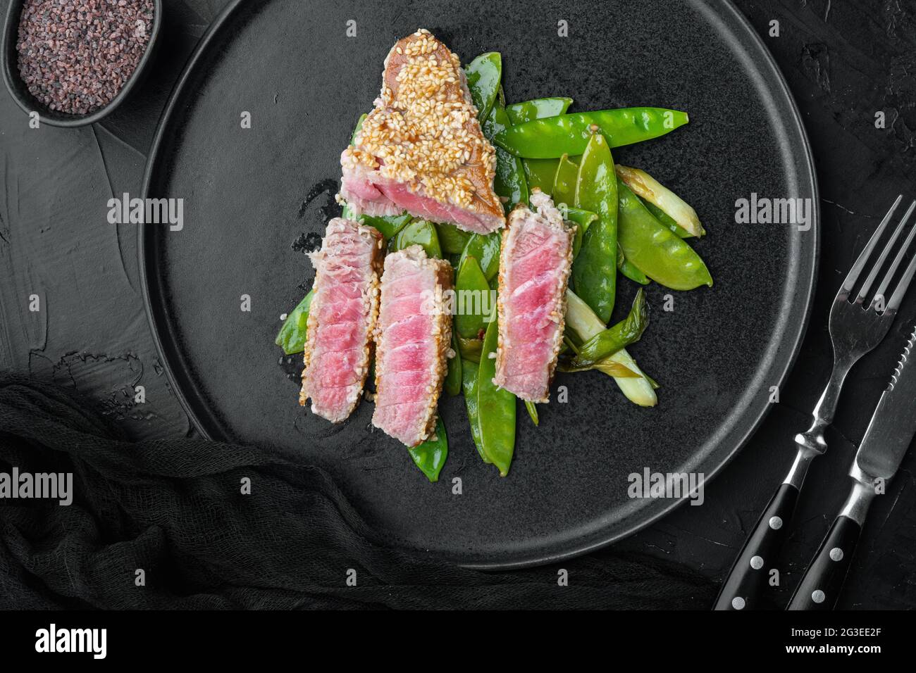 Bistecca di tonno rosso raro alla griglia con cipolle e piselli a  bottoncino di zucchero, su piatto, su fondo di pietra nera, vista dall'alto  piatto Foto stock - Alamy