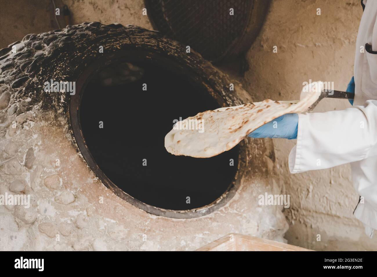 l'uomo invecchiato fa il pane tradizionale nel vecchio forno rotondo della pietra nel villaggio rurale. Cucina dell'Asia centrale. Pane caldo. Foto Stock