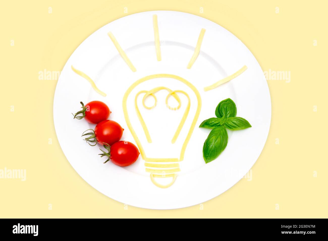 Composizione creativa del cibo: Vista dall'alto di un piatto bianco con un simbolo luminoso della lampadina fatta di pasta bollita, pomodori ciliegini e foglie di basilico isolati Foto Stock