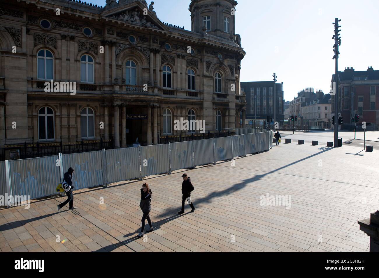 Il pubblico mantiene la loro distanza l'uno dall'altro e getta lunghe ombre nella luce del primo mattino in Piazza Regina Vittoria nel centro di Hull City come il C. Foto Stock