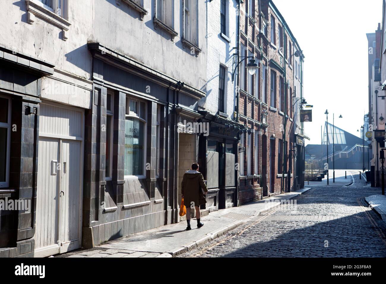 Una donna torna indietro dai negozi nella strada ora deserta e vuota della città vecchia di Hull sono del centro di Hull City, come l'epidemia di Coronavirus peggiora Foto Stock