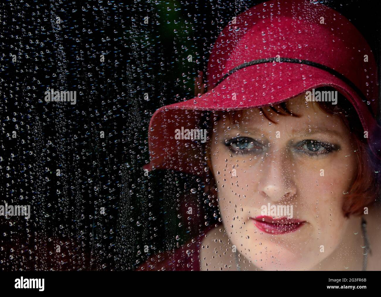 Donna che guarda attraverso la finestra coperta di gocce di pioggia. Foto Stock